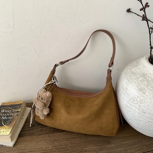 Detail of a brown suede croissant bag with a cute teddy bear charm on a wooden table