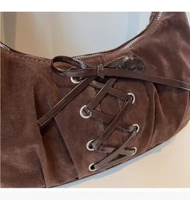 Detail of dark brown suede shoulder bag with cross-lace design and metal eyelets