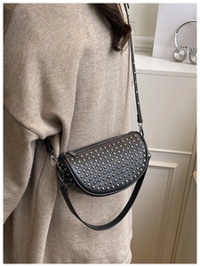 Detail of black crossbody bag with silver studs on a beige knit sweater background