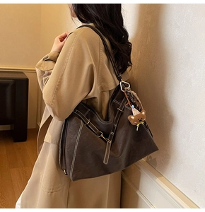 Detail view of large dark brown leather tote bag with white stitching and bear charm