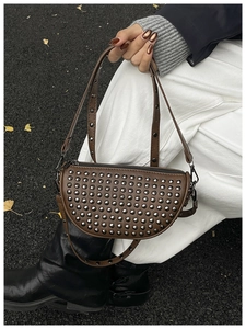 Brown leather shell bag with silver studs and adjustable shoulder strap worn by model