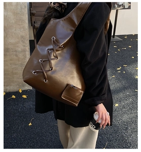 Detail of dark brown glossy leather tote with cross-tie design and mini pouch attachment