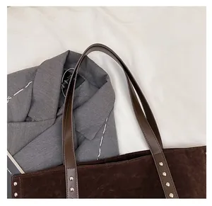 Detail of dark brown suede tote bag with silver studs on textured office blazer