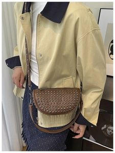 Brown saddle bag with silver rivet details worn with a beige jacket and polka dot skirt