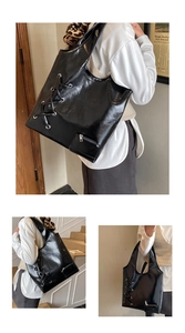 Detail of black glossy tote bag featuring decorative silver eyelets and cross lacing