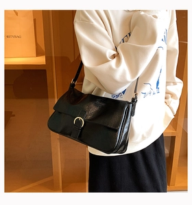 Close-up of black glossy shoulder bag with vintage gold buckle on a stylish model