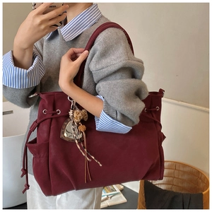Macro detail of burgundy tote bag featuring drawstring closure and leopard print charm