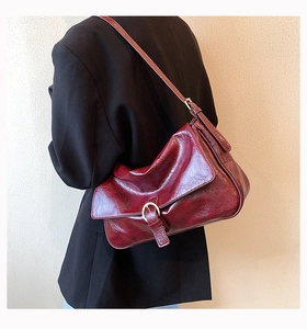 Detail of burgundy leather shoulder bag with glossy oil-wax texture and buckle flap