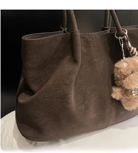 Detail of brown tote bag showing matte leather texture, stitching, and cute bear charm