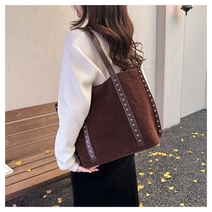Detail of dark brown suede tote bag featuring silver rivet studs and a leather shoulder strap