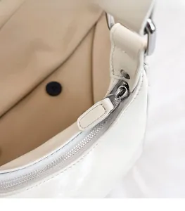 Detailed view of the smooth silver zipper and leather puller on white underarm bag
