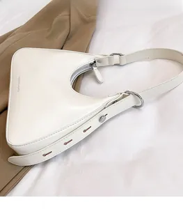 Detail of white baguette bag showing silver rings and adjustable strap with metal eyelets