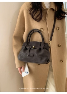 Detail of dark brown retro shoulder bag with decorative buckle on light camel wool coat