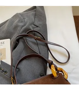 Detail of adjustable leather strap and matte gold chain handle on brown suede boston bag