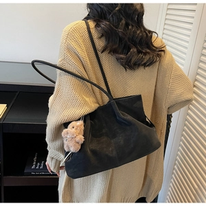 Detail of black leather tote bag with plush bunny charm on beige knit sweater outfit