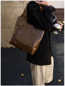 Detail of dark brown tote bag with metal eyelets, lace-up side and functional zipper pocket