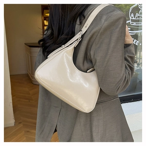 Detail view of cream-colored hobo bag with silver buckle on a stylish model shoulder