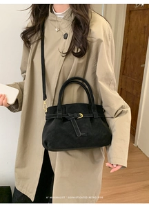 Detail of a black minimalist retro suede bag with a gold buckle on a model in a trench coat