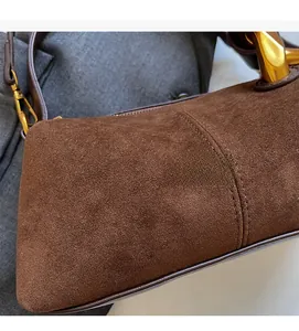 Detail of brown suede texture with white stitching and shiny gold metal hardware accents