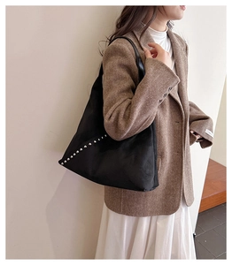 Detail of suede tote bag with silver studs on shoulder of model in herringbone blazer