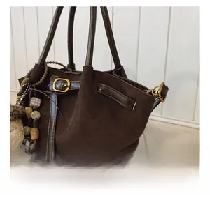 Detalle de bolso de ante marrón oscuro con hebillas metálicas y colgantes decorativos