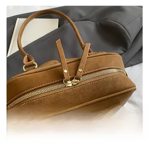 Detail view of smooth double gold zippers and long leather pulls on brown pillow bag