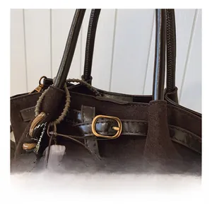 Detalle de bolso de ante marrón oscuro con hebilla dorada y amuleto de leopardo