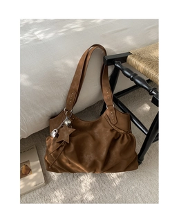 Detail of a brown suede tote bag with silver studs and heart-star shaped metal charms