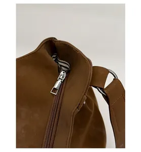 Detail view of silver metal zipper and striped lining on brown suede shoulder bag