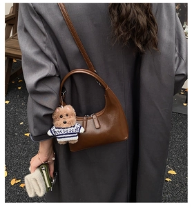 Détail du sac demi-lune marron avec pendentif chien sur un blazer gris foncé