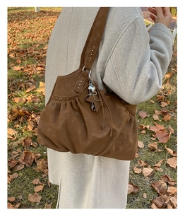Close-up of brown suede tote bag with metallic studs and star charms on an autumn background