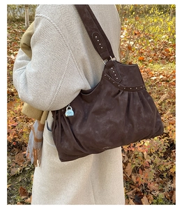 Close-up of vintage brown suede tote with silver rivets and lock charm in outdoor setting