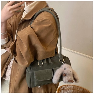 Detail of dark green suede Boston bag with flap pockets and plush rabbit pendant