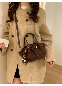 Détail d'un sac cabas rétro en daim marron foncé avec boucle en cuir et pompon coloré