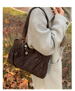 Detail of dark brown suede shoulder bag with rivets and metal charms in an outdoor setting
