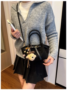 Detail of black suede handbag featuring a metal buckle and a cute teddy bear plush charm