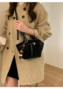 Détail du sac cabas en daim noir avec breloque bohème et finitions dorées sur manteau