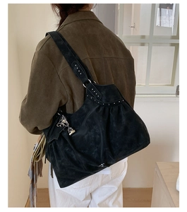 Detail of black suede hobo bag with silver studs and a metallic bow bell charm