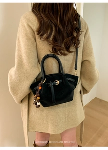 Détail d'un sac à main en daim noir avec perles décoratives sur fond de manteau en laine beige