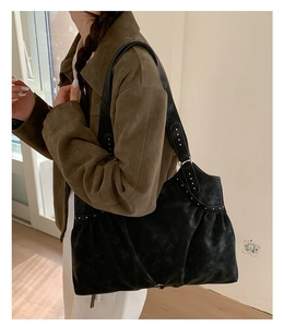 Detail of black suede hobo bag with silver rivets and pleated texture on wide shoulder strap