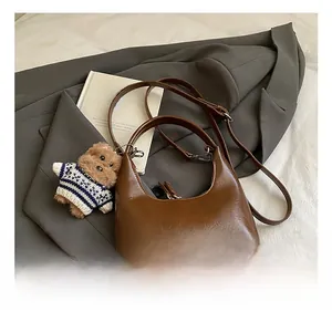 Détail d'un sac hobo en cuir marron brillant avec bandoulière et charm ours mignon