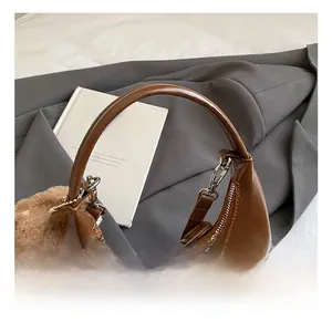 Détail d'un sac hobo marron brillant avec poignée incurvée et breloque boule en peluche