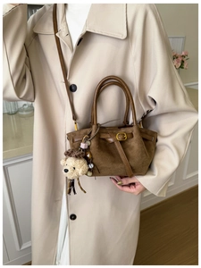 Detail of a brown suede handbag featuring a plush dog charm and colorful beaded strap