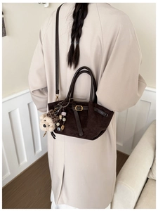 Detail of dark brown suede handbag featuring a plush bear charm and leather buckle straps