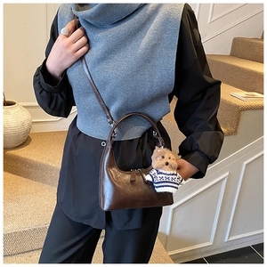 Détail du sac à bandoulière en cuir brillant marron foncé avec un charmant ours en peluche