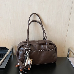 Detalle de bolso de cuero marrón oscuro con textura tejida y amuleto de perro decorativo