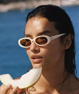 Outdoor close-up of white oval frame sunglasses with brown lenses and metal trim details