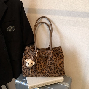 Detail of leopard print tote bag featuring brown leather handles and a plush bear charm