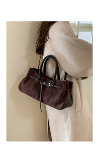 Détail du sac à main en daim marron foncé porté avec un manteau en laine beige au ton chaud