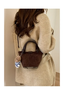 Detail of dark brown suede bucket bag with leather handles and cute teddy bear charm